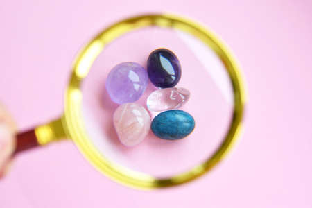 Close up of semi-precious stones of different colors by magnifying glass. Amethyst, rose quartz,...