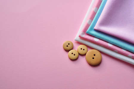 Cotton fabric of different colors, patterns and colored ribbons and wooden buttons on a pink background. Space for text, top viewの写真素材