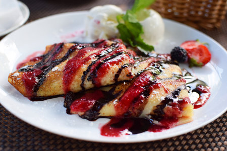 Crepes stuffed with fruit and covered with chocolate and berry syrups. Served with ice cream balls and strawberries. Thin pancakes, blini. Sweet dessert.の写真素材
