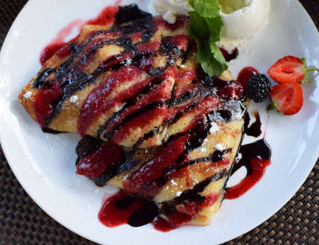 Crepes stuffed with fruit and covered with chocolate and berry syrups. Served with ice cream balls and strawberries. Thin pancakes, blini. Top viewの写真素材