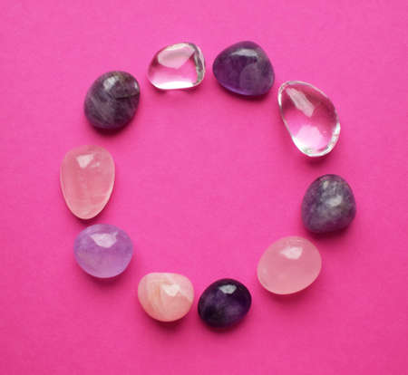The circle is lined with natural minerals. Semi-precious stones of different colors processed. Amethyst and rose quartz. Frame of gems on bright pink background.の写真素材