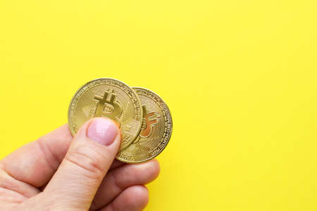 Two metal bitcoin coins in hand on a yellow background. Bitcoin BTC Cryptocurrency coins. Stock market concept.の写真素材