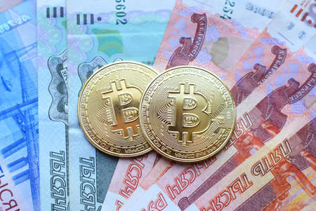 Metal shiny bitcoin crypto currency coins on rubles banknotes. Electronic money concept.