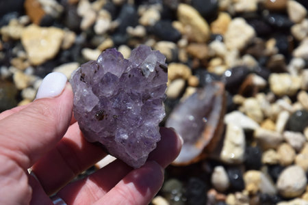 Beautiful purple amethyst crystals in a female hand. Druse of amethyst in the shape of a heart against the background of other precious stones.の写真素材