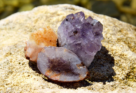 A beautiful druse and geode of amethyst and druse of citrine lie on a stone. Crystals of semi-precious stones in the sun.の写真素材