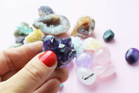Beautiful dark purple amethyst crystals in hand. Druse of amethyst in a woman's hand against the background of other precious stones.の写真素材