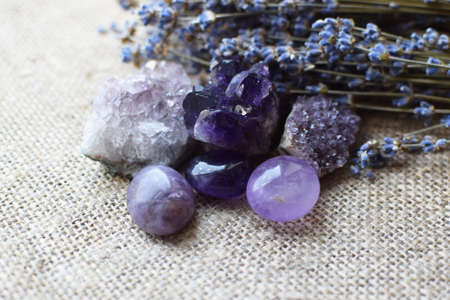 Beautiful amethyst stones and amethyst druze with a dry bouquet of lavender against a background of coarse burlap fabric. Magic amulets.の写真素材
