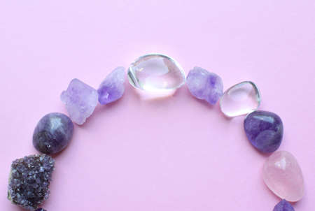 The circle is lined with natural minerals. Semi-precious stones of different colors, raw and processed. Amethyst and rose quartz on a pink background.の写真素材
