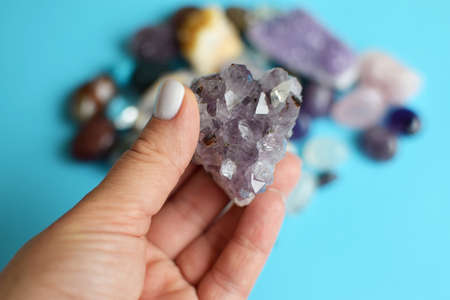 Beautiful purple amethyst crystals in hand. Druse of amethyst in a woman's hand against the background of other precious stones. selective focus.の写真素材
