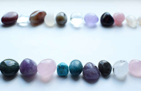 Frame made of semi-precious stones of different colors. Amethyst, rose quartz, agate, apatite, aventurine, olivine, turquoise, aquamarine, rock crystal lie in two rows on a white background.の写真素材
