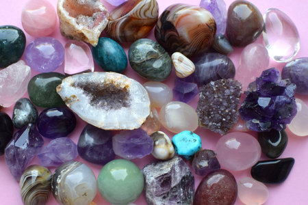 Semi-precious stones of different colors. Amethyst and amethyst druse crystals, rose quartz, agate, apatite, aventurine, olivine, turquoise, aquamarine, rock crystal on a pink background.の写真素材