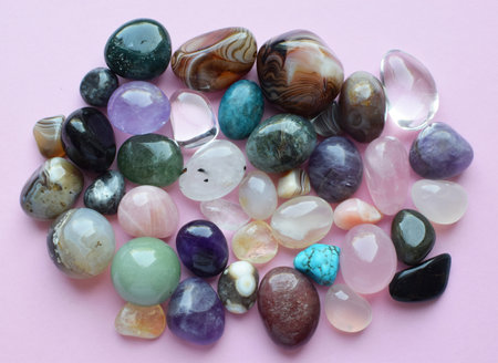 Semi-precious stones of different colors. Amethyst and amethyst druse crystals, rose quartz, agate, apatite, aventurine, olivine, turquoise, aquamarine, rock crystal on a pink background.の写真素材
