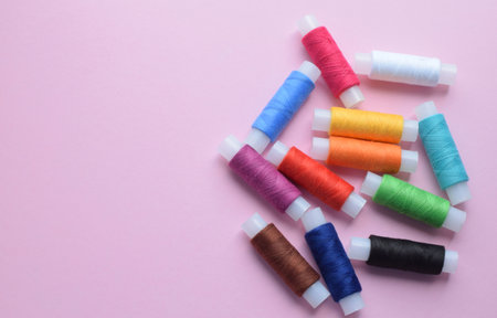 Sewing with colored threads on a pink background. Cotton threads in spools are laid out in rainbow colors. copyspace. View from aboveの写真素材