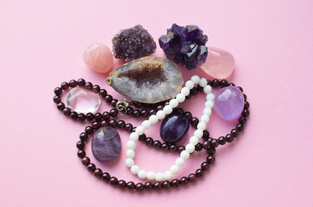 Garnet beads and amethyst, rose quartz and rock crystal crystals on a pink background.の写真素材