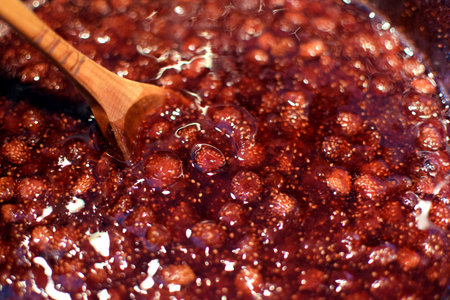 Making strawberry jam at home. Wild strawberry jam is boiled in a saucepan and stirred with a wooden spoonの写真素材