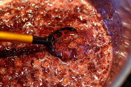 Making strawberry jam at home. Strawberry jam is boiled in a saucepan and stirred with a wooden spoon with Khokhloma paintingの写真素材