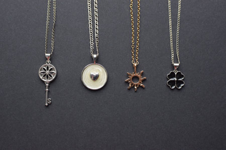 Jewelry pendants on chains in the form of a key, heart, sun and clover on a gray background.の写真素材