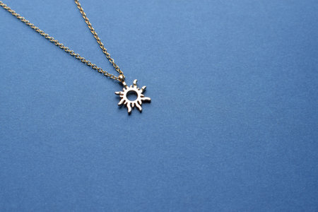 Jewelry golden pendant on a chain in the form of a sun on a blue background.の写真素材