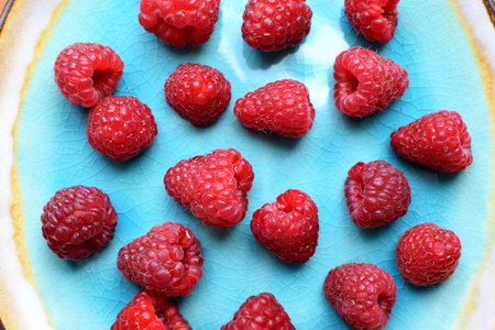 Ripe red raspberries on a blue plate on a wooden background. Sweet raspberry background. Berries...