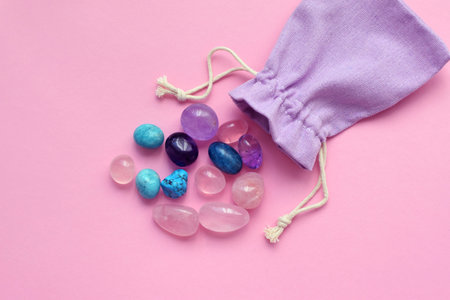 Beautiful natural semi-precious stones: rose quartz, amethyst, turquoise and kyanite, in a fabric bag on a pink background.の写真素材