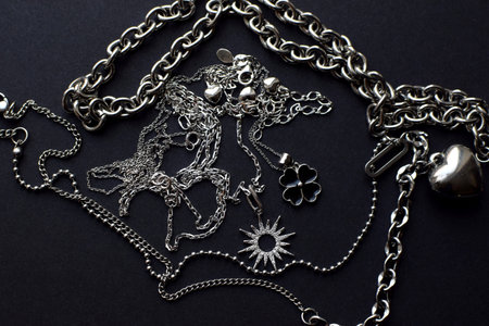Silver jewelry pendants on a chain in the form of a sun, star and clover on a dark background.