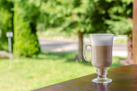 Glass cup of latte coffee on the wooden table outdoors.の写真素材