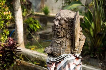 an ancient stone deity with a beard, curly hair, round eyes, large teeth and fangs, located in the tropical forest of Bali. The horizontal frame.の写真素材