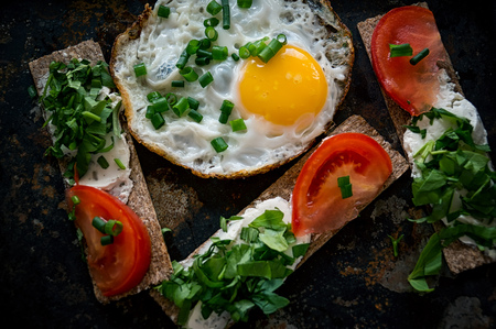 Scrambled eggs and sandwiches with cheese, greens and tomato in a rustic style.