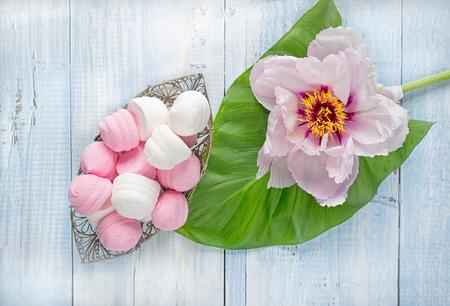Marshmallows in a vase next to peony flower on a green leaf on a light wooden background.の写真素材