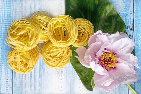 Nest pasta on a blue wooden background next to a large beautiful pink peony flower.の写真素材