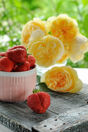 Ripe strawberry in a Cup of pink ceramic on a background of yellow roses. The vertical frame.の写真素材