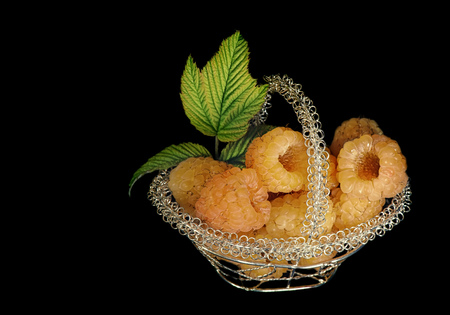 Yellow raspberry in openwork metal basket on a black background.