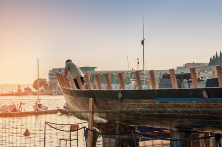 Workshop for restoration of ships on the shores of the Adriatic sea. Man repairs a boat at dawn at sunrise.の写真素材