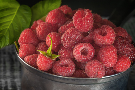 Ripe red raspberries lying in a metal dish close-up. The horizontal frame. .