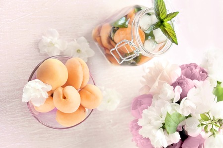 Detox with pieces of peach and apricot, with ice and mint in a glass container, and apricots close-up. A refreshing drink on the background of bouquet of pink peonies.の写真素材