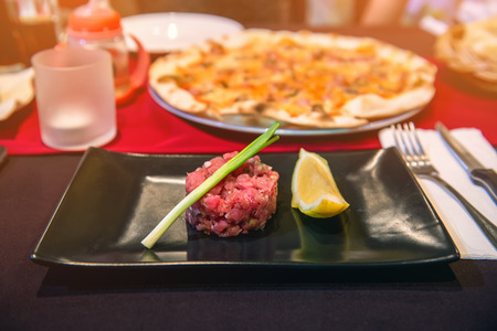 Portion of their beef tartare with lemon wedges on black plate on table in cafe.の写真素材
