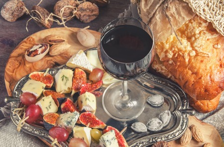 A glass of dry red wine and Italian Focaccia bread with cheese and a cheese platter with figs and Gorgonzola, brie, DorBlu and grapes. Selective focus. The horizontal frame.の写真素材