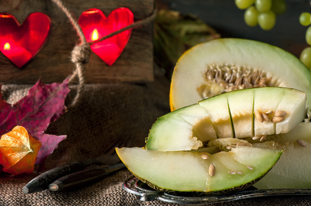 Large juicy chunks of ripe melon on the background of beautiful candles and bunches of grapes. Close-up.の写真素材