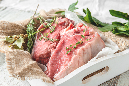 Cuts of beef for grilling on a wooden cutting Board with spinach, rosemary and Provencal herbs for the marinade in a rustic style. The horizontal frame.の写真素材