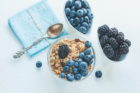 Ripe blueberries and blackberries on white background in white ceramic bowls with granola. Morning...