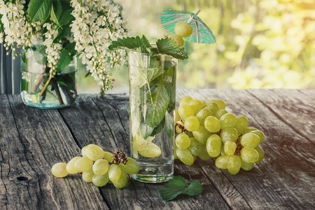 Detox water mint, grape juice and ice in a glass on a background of a bouquet of cherry and grapes in a Sunny day.の写真素材