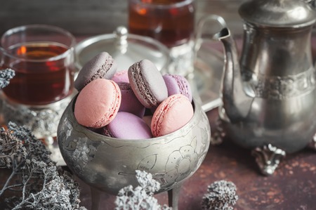 Freshly baked macaroons on metal plate with small white flowers and tea appliances composition on wooden background. Selective focus. Copy space.の写真素材