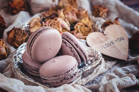 Freshly baked macaroons on a metal plate with small flowers and a wooden heart . Selective focus.の写真素材