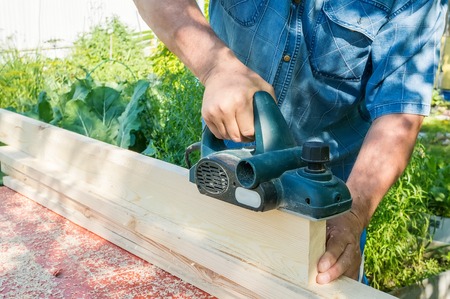 The master sharpens the wooden panel with an electric sander on a Sunny day in the garden. Close up.
