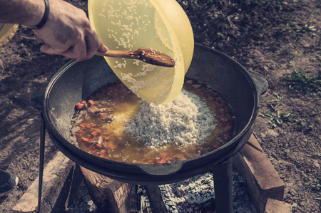Hands put the rice in a large cauldron for cooking pilaf in the open air on a Sunny day. A horizontal frame.の写真素材