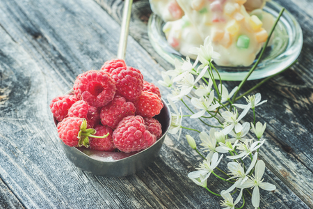 Ripe fresh raspberries in a white pot in a rustic style with small white clematis flowers close-up.の写真素材