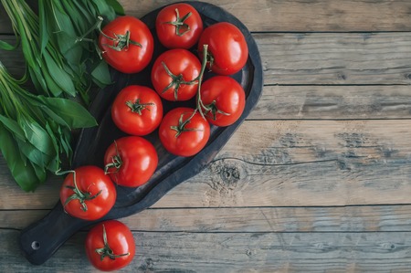 A large branch of ripe red tomatoes on a wooden Board with leaves of ramson in a rustic style.の写真素材