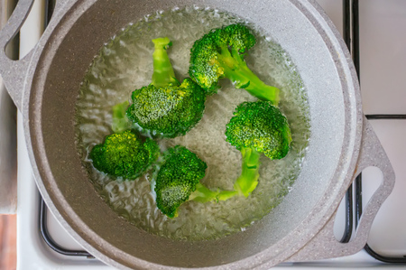 Pieces of fresh broccoli cook in boiling water in a saucepan. Healthy food for children and diet. Close up.の写真素材