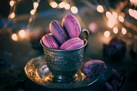 Freshly baked macaroons on a silver metal Cup with bokeh from the lights on the wooden background....