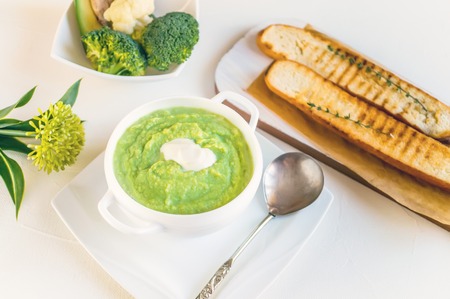 Cream soup of broccoli, avocado and cauliflower with whipped cream on a wooden table. The view from the top.の写真素材
